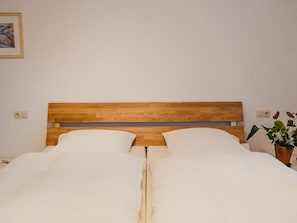 A bed with a wooden headboard, white bedding, and a potted plant on the side.