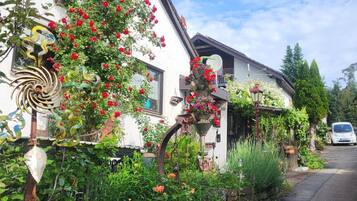 A residential street with a white house featuring a garden with red flowers and a decorative metal sculpture.