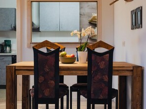 Un comedor con una mesa y sillas de madera, un bol de fruta y un florero con flores.