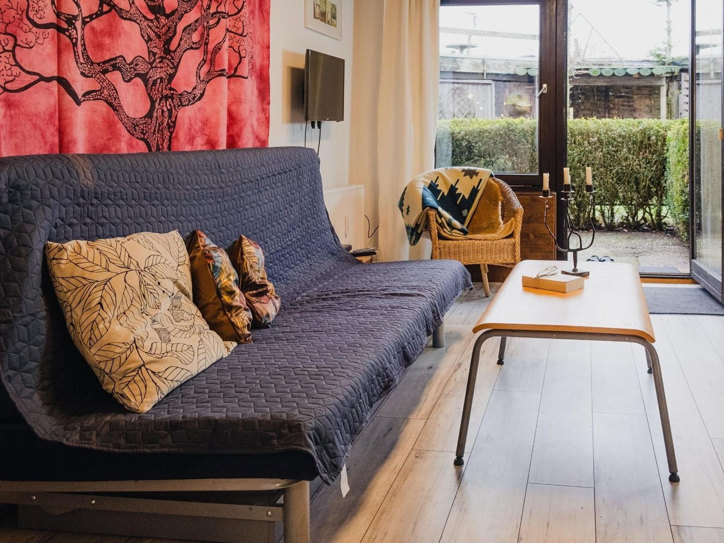 A modern living room with a dark blue sofa, patterned cushions, a wooden coffee table, and a wicker chair.