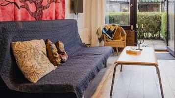 A modern living room with a dark blue sofa, patterned cushions, a wooden coffee table, and a wicker chair.