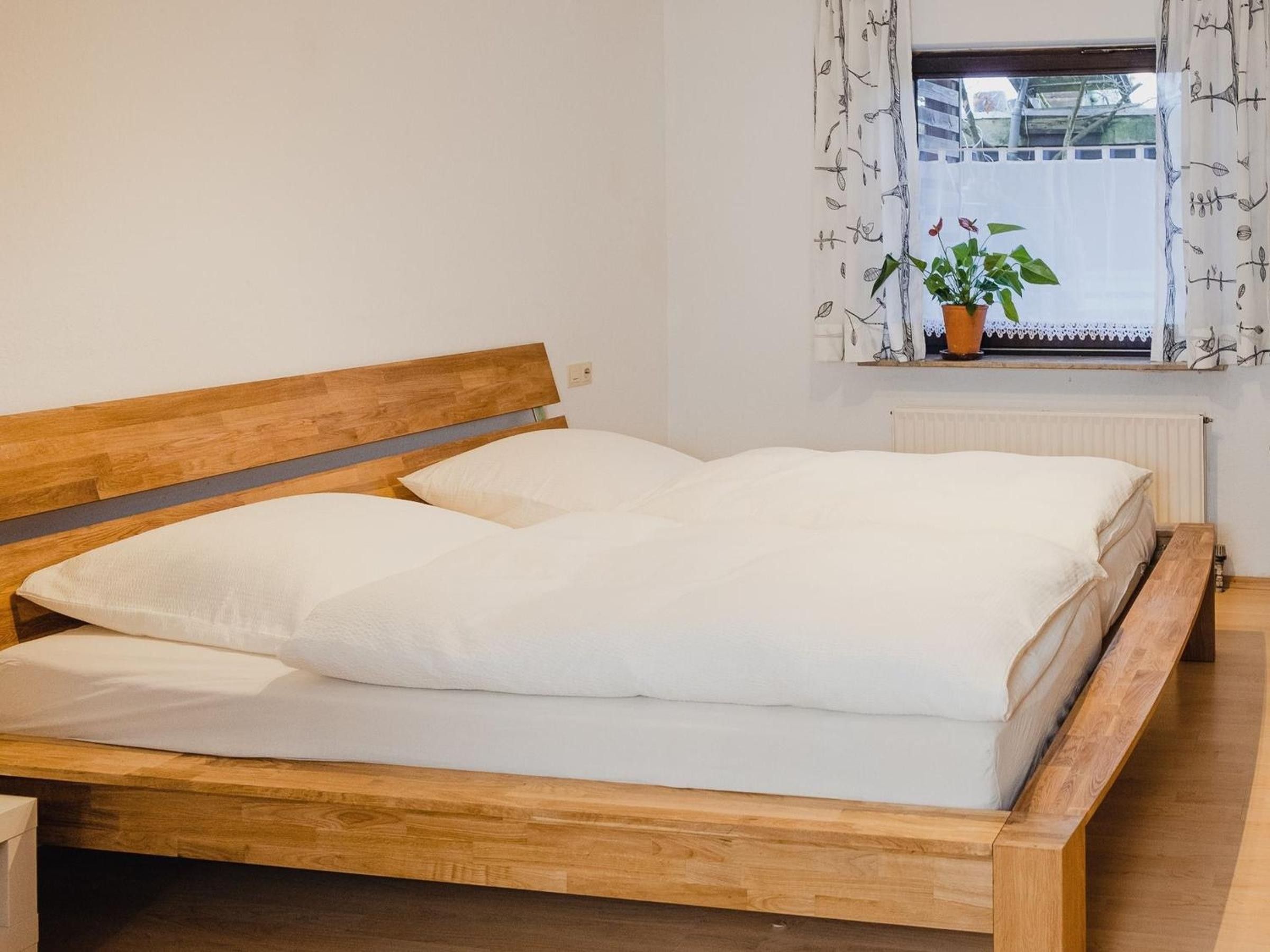 Una cama de madera con ropa de cama blanca en una habitación con ventana y radiador.