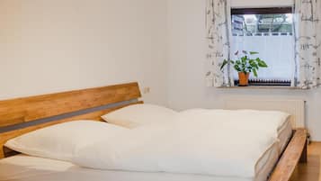 Una cama de madera con ropa de cama blanca en una habitación con ventana y radiador.