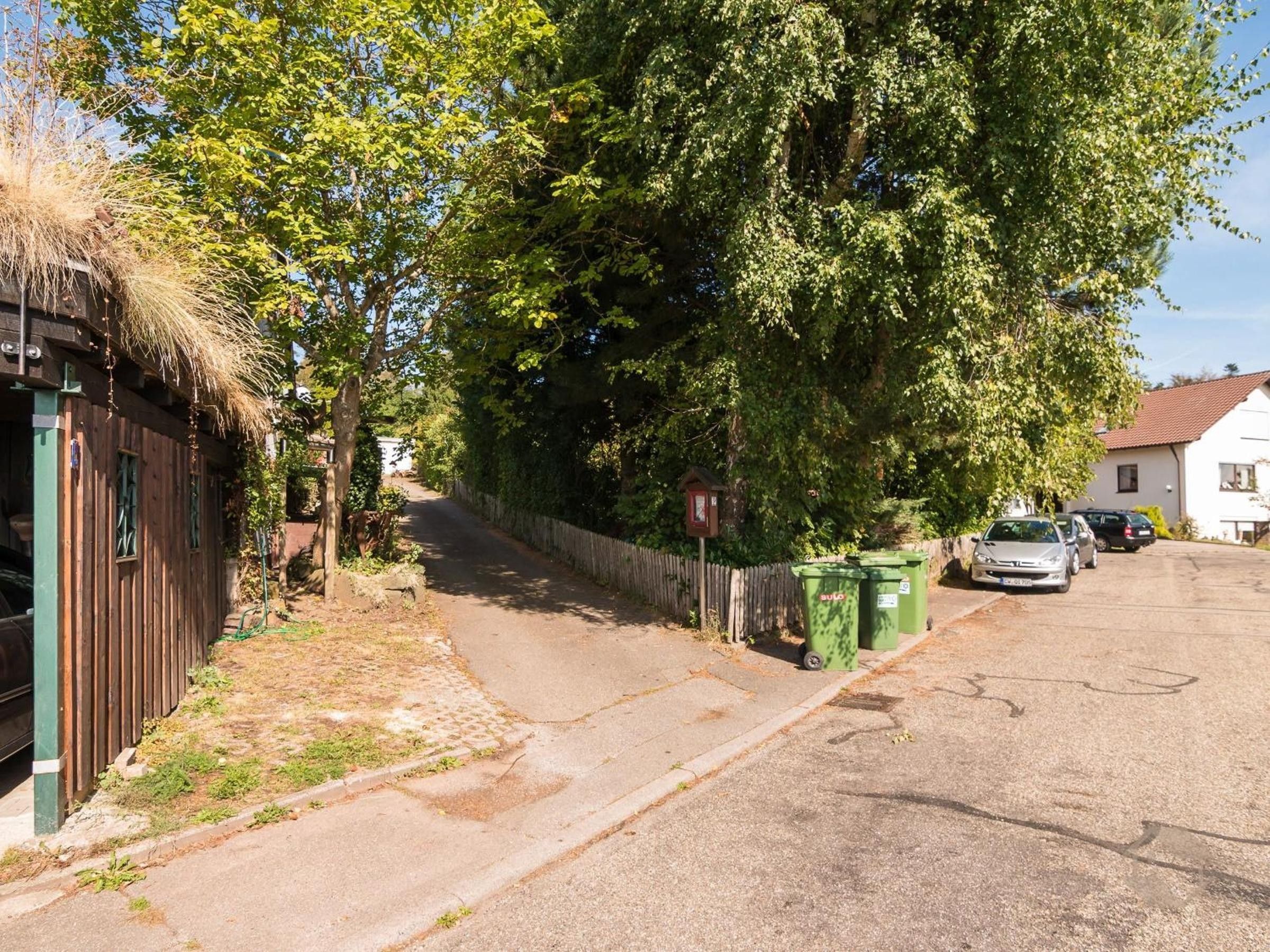 Una calle residencial con una casa de madera, una cerca y coches aparcados.