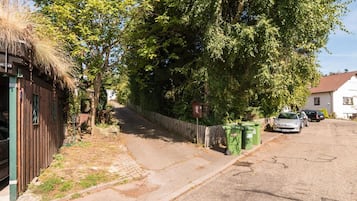 Una calle residencial con una casa de madera, una cerca y coches aparcados.