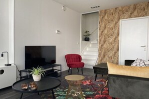 Een moderne woonkamer met een flatscreen televisie, een rode fauteuil, een bank, een salontafel en een trap met een behang.