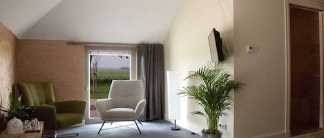 A bedroom with a large window, a chair, a bedside table, and a potted plant.