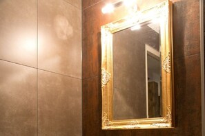 Een spiegel met een sierlijk gouden frame bevestigd aan een wand met een donkere, structuurrijke oppervlakte.