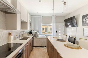 A modern kitchen with a central island, a dining area with a long table, and a view of the outside. - 1BedsQueen+Fullsize NearDowntown~Stockyards~TCU (Fort Worth)