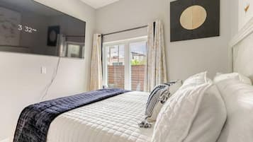A bedroom with a bed, a window with curtains, a wall clock, and a framed artwork.