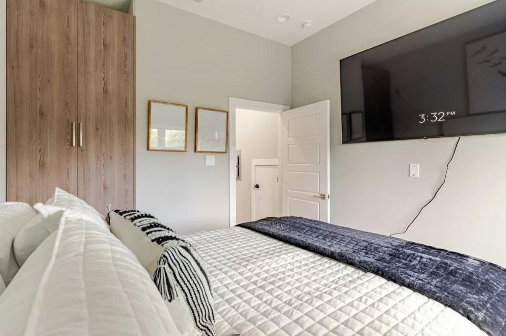 A bedroom with a bed, a wardrobe, a television mounted on the wall, and a door leading to another room.