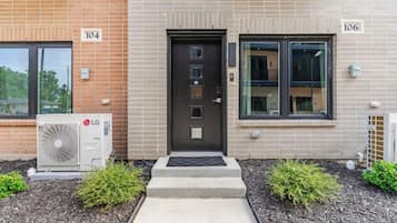A building with numbered doors, an air conditioning unit, and a small garden area.