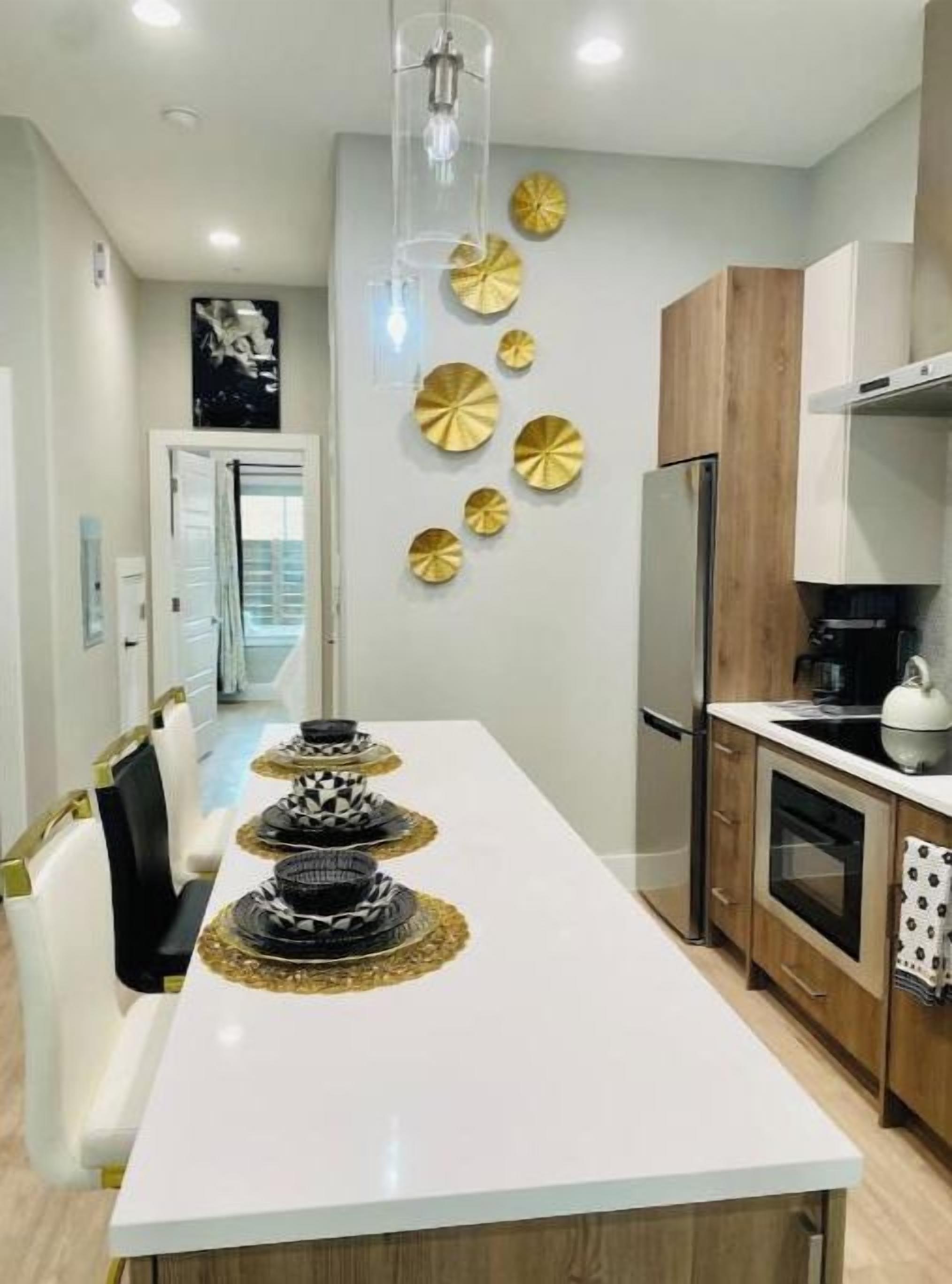 Une cuisine moderne avec un plan de travail blanc, des appareils en acier inoxydable et des éléments décoratifs dorés sur le mur.