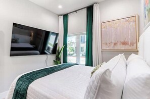 A hotel room with a bed, a flat-screen TV mounted on the wall, a window with curtains, and a painting on the wall. - 2Near Downtown~Stockyards~DFW Zoos~6 Flags~2 Beds! (Fort Worth)
