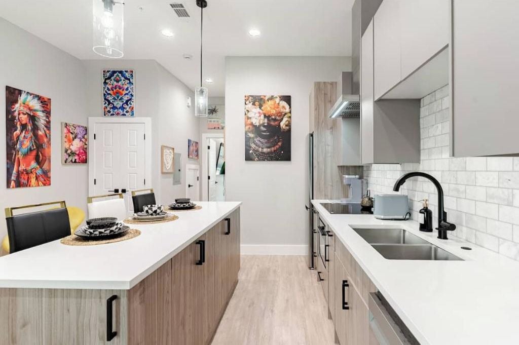 A modern kitchen with white countertops, a central island, and a sink on the right.