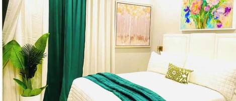 Un dormitorio con una cama, una cortina verde, un cuadro y una planta en maceta.