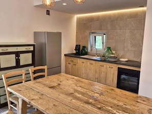 A kitchen with a wooden table, cabinets, a refrigerator, and a window. - Racconti di Puglia B&B (Polignano a Mare)