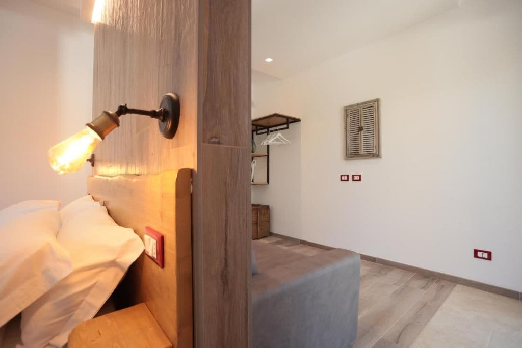 A room with a bed, a wooden headboard, a wall-mounted light fixture, a wooden bench, and a small table.