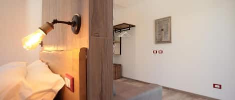Une pièce comprenant un lit, une tête de lit en bois, un luminaire fixé au mur, un banc en bois et une petite table.
