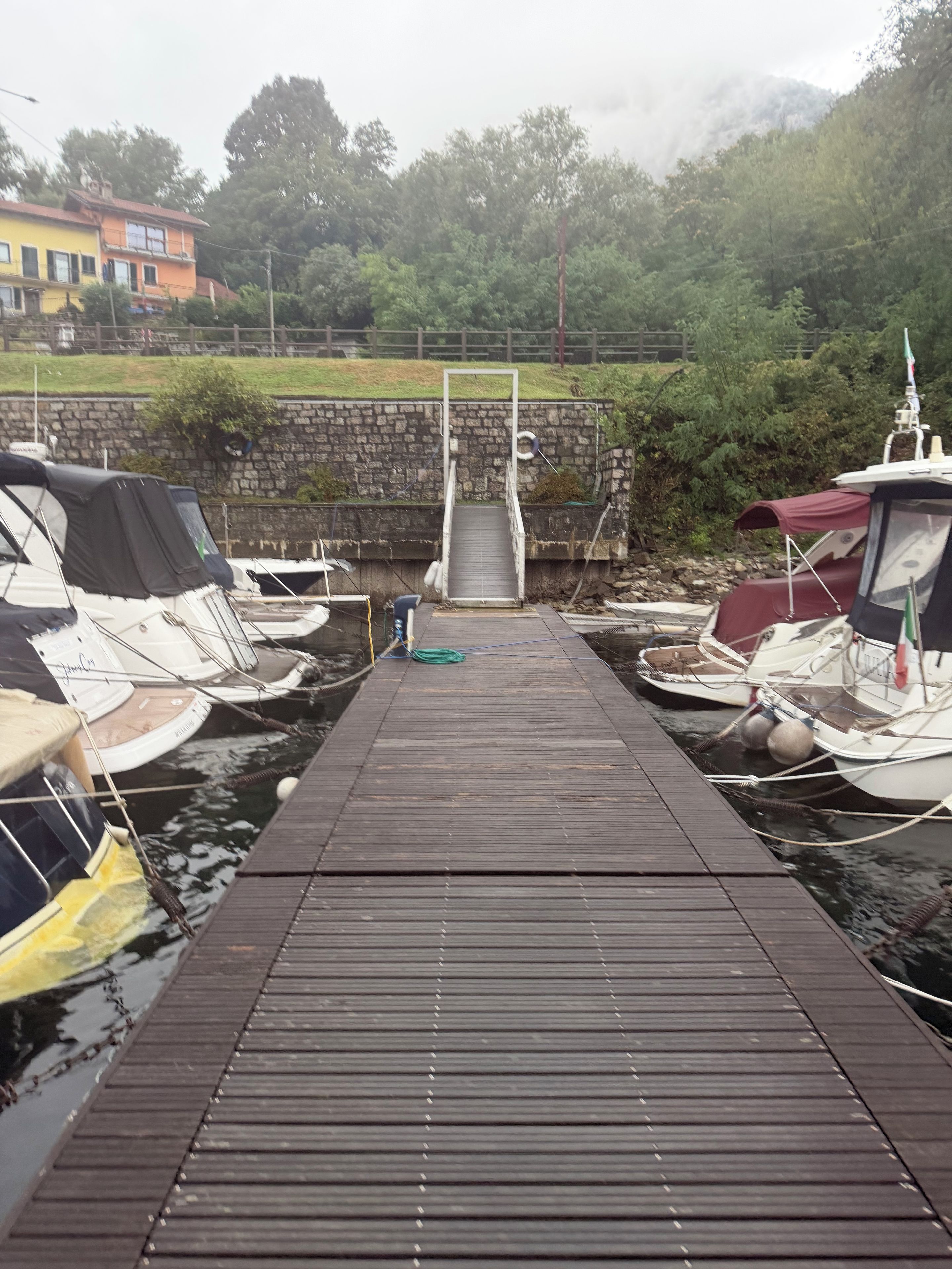 Une jetée en bois mène à un mur de pierre, de part et d’autre duquel sont amarrés des bateaux.