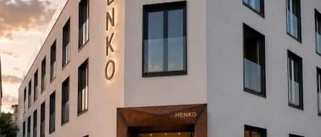A modern building with the name 'HENKO' on its facade, featuring a glass entrance and multiple windows.