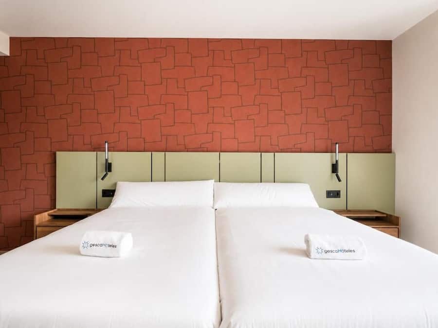Una cama doble con ropa blanca, dos mesitas de noche y un cabecero con diseño de ladrillo.
