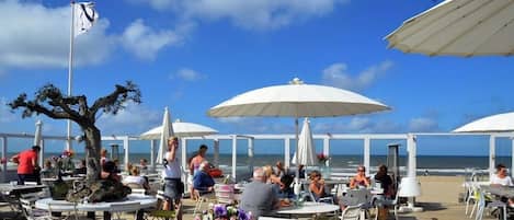 An outdoor dining area with tables and umbrellas, overlooking the beach.