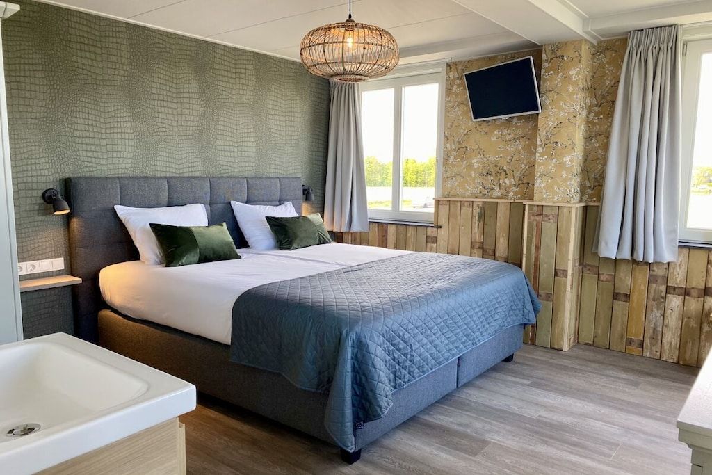 Ein Schlafzimmer mit einem Bett, einem Nachttisch, einem an der Wand montierten Fernseher und einem Fenster mit Vorhängen.