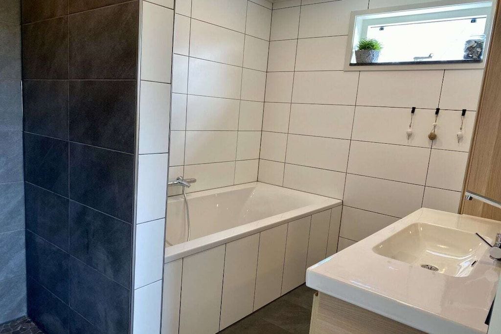A bathroom with a bathtub, a sink, and a window with a plant.