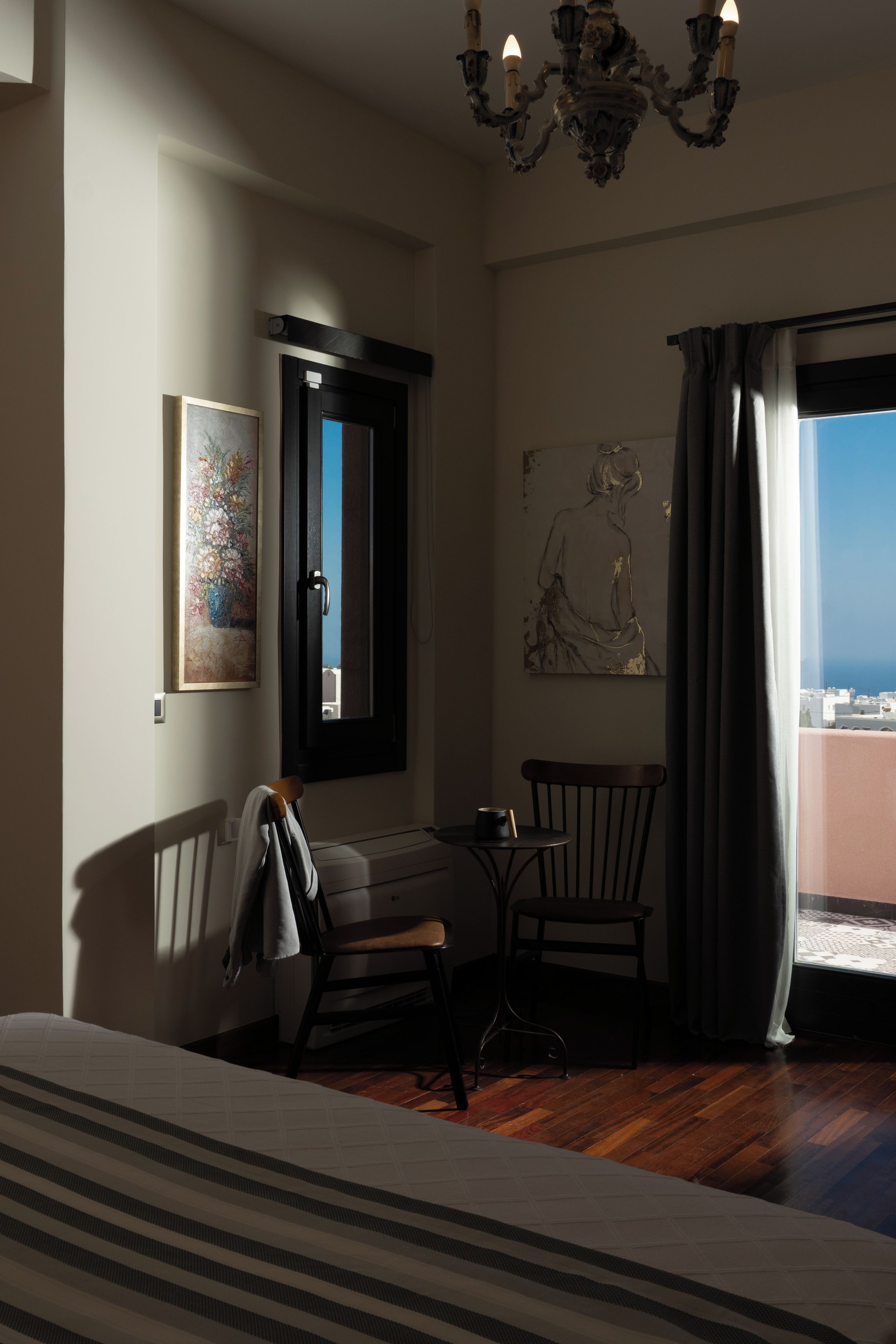 Een hotelkamer met een bed, een stoel, een klein tafeltje, een schilderij en uitzicht op zee.