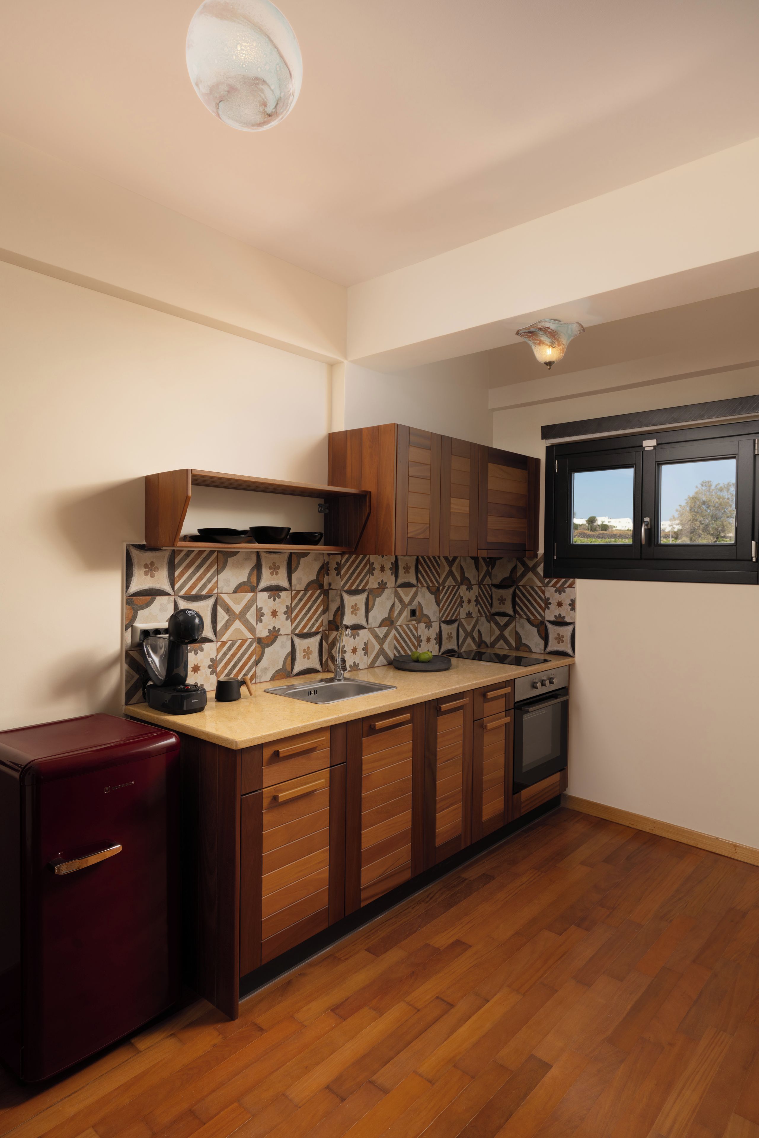 A compact kitchen with wooden cabinets, a built-in oven, and a coffee machine.