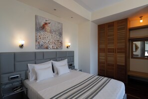 A hotel room with a large bed, a headboard, bedside tables, a nightstand, a wall-mounted painting, two wall sconces, and a wooden wardrobe with a mirror.