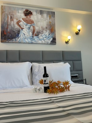 A hotel room with a bed, a painting on the wall, and a bottle of wine on the bed.