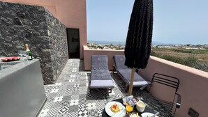 Une terrasse avec une table préparée pour le petit-déjeuner, des chaises longues et une vue sur la mer.