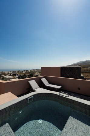 A rooftop pool with lounge chairs and a view of a coastal town.