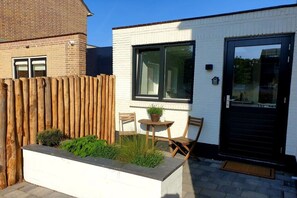 A white building with a black door, a window, and a wooden fence. - Studio Tol Zandvoort (Zandvoort)