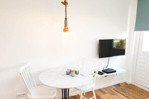 A room with a round table, white chairs, a mounted television, and a small shelf with a remote control. - Studio Tol Zandvoort (Zandvoort)