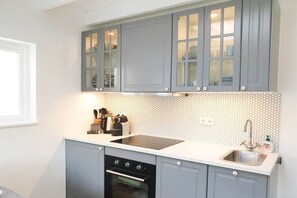 A kitchen with grey cabinets, a white countertop, a sink, and a tiled backsplash. - Studio Tol Zandvoort (Zandvoort)