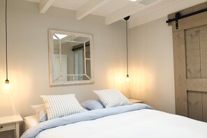 A bedroom with a bed, two bedside tables, a mirror, and a wooden door. - Studio Tol Zandvoort (Zandvoort)