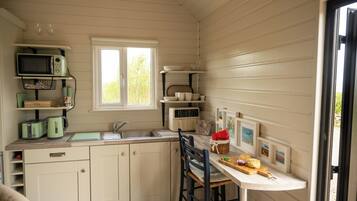 A compact kitchen with a sink, a microwave, and a toaster. There is a window providing natural light, and a dining area with a chair and a table.