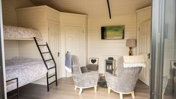 A compact room with a bunk bed, two armchairs, a small table, a heater, and a painting on the wall.