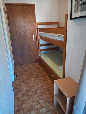 Ein kleiner, kompakter Raum mit einem hölzernen Etagenbett, einer Tür und einem kleinen Holzregal.