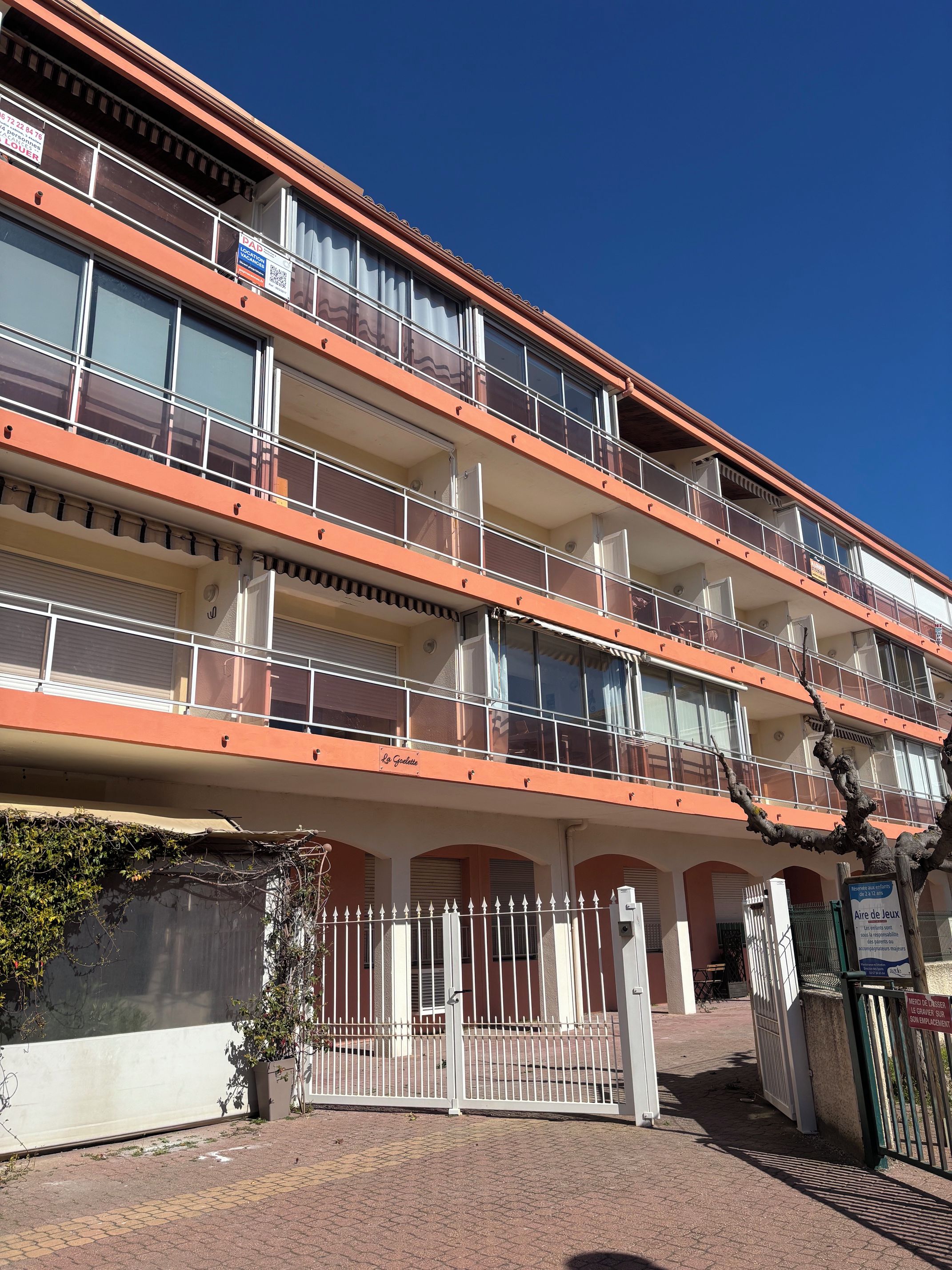 Un immeuble à plusieurs étages doté de balcons, d’une entrée sécurisée et surplombant un ciel dégagé.