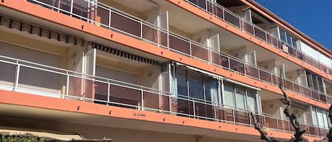 A multi-story building with balconies, a gated entrance, and a clear sky.