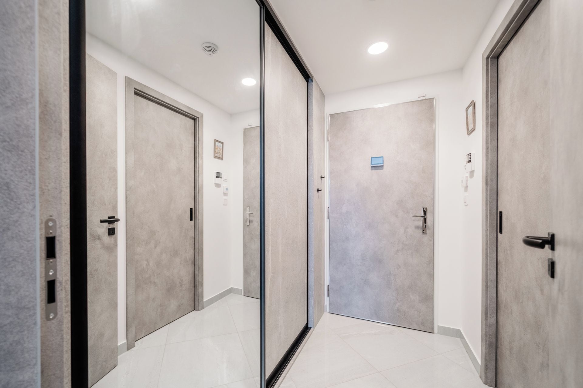 A modern hallway with mirrored walls, a tiled floor, and doors with electronic locks and keypads.