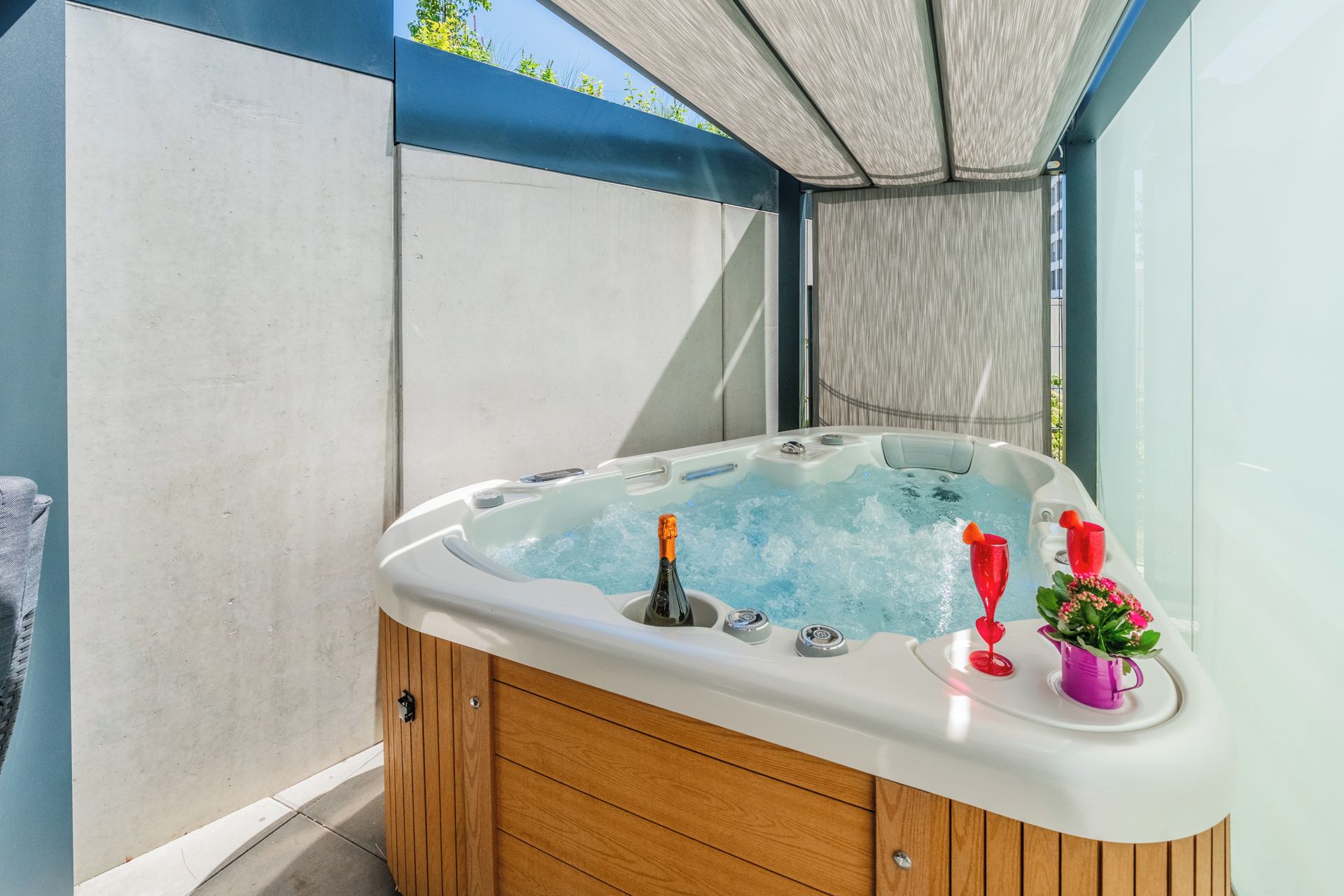 A hot tub with a wooden cabinet, a bottle, and two red glasses.