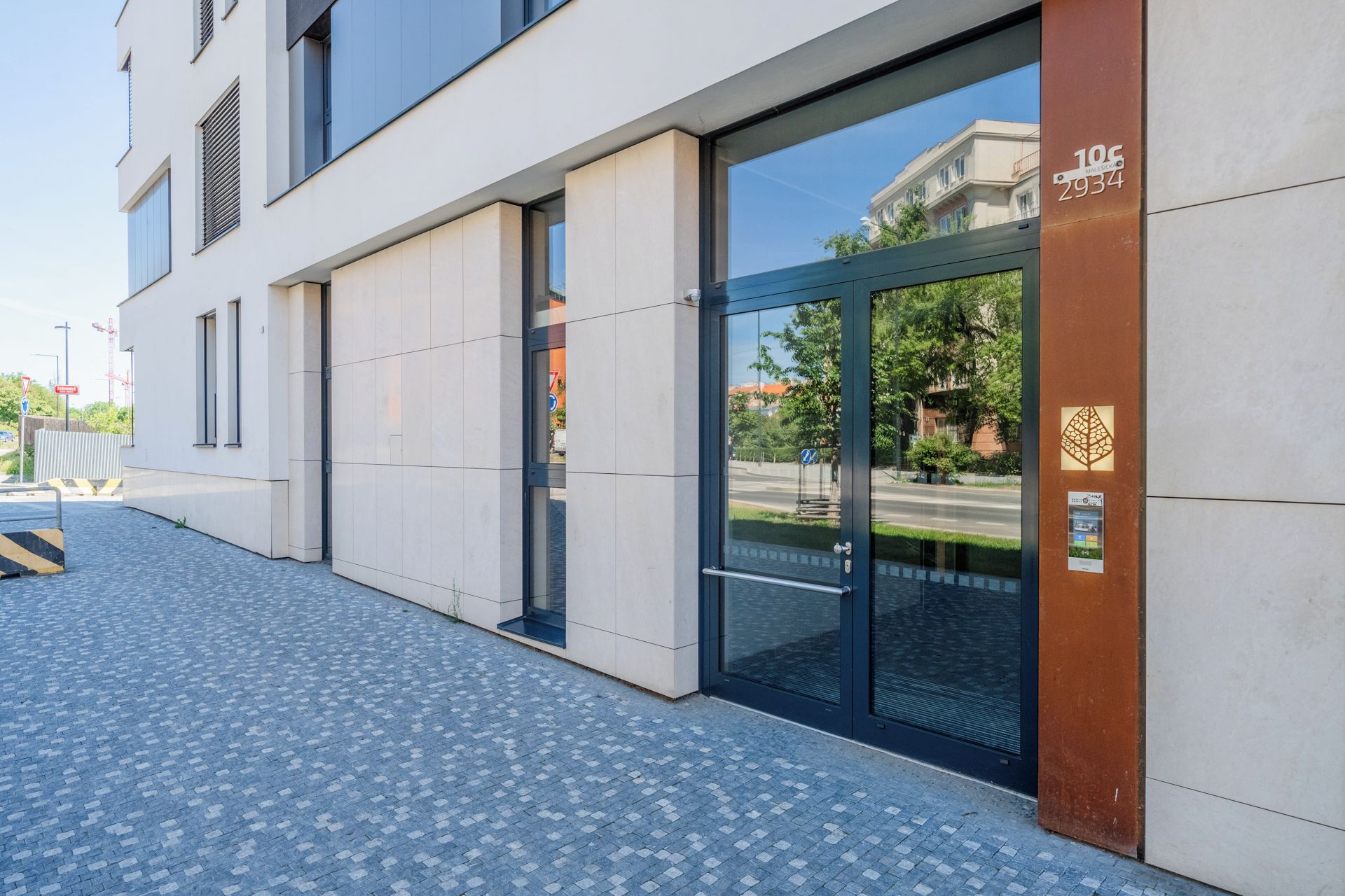 Ein moderner Gebäudeeingang mit Glastür, Metallgitter und einem gepflasterten Weg.
