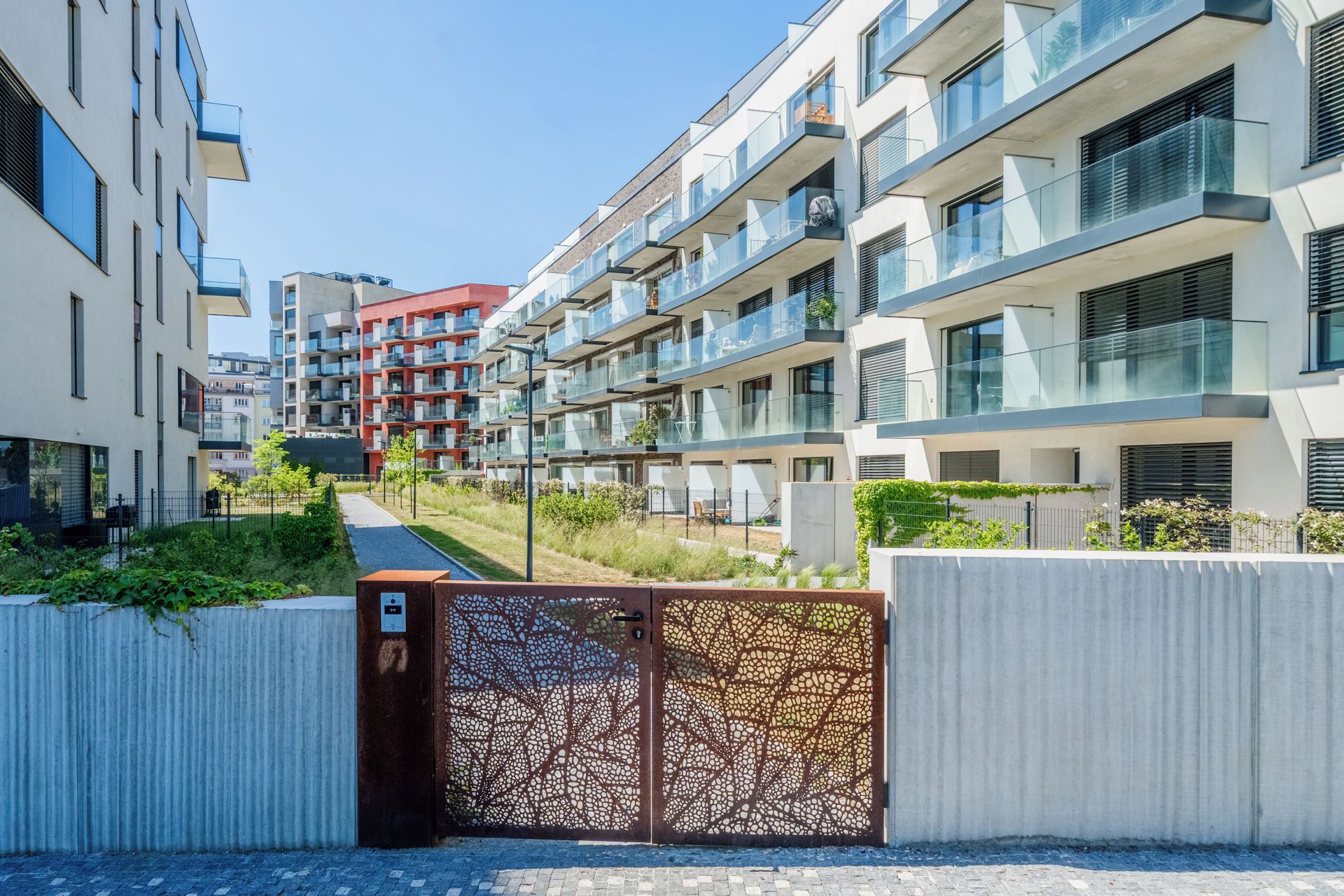 A modern apartment complex with multiple balconies, a gated entrance, and a pathway leading to the buildings.