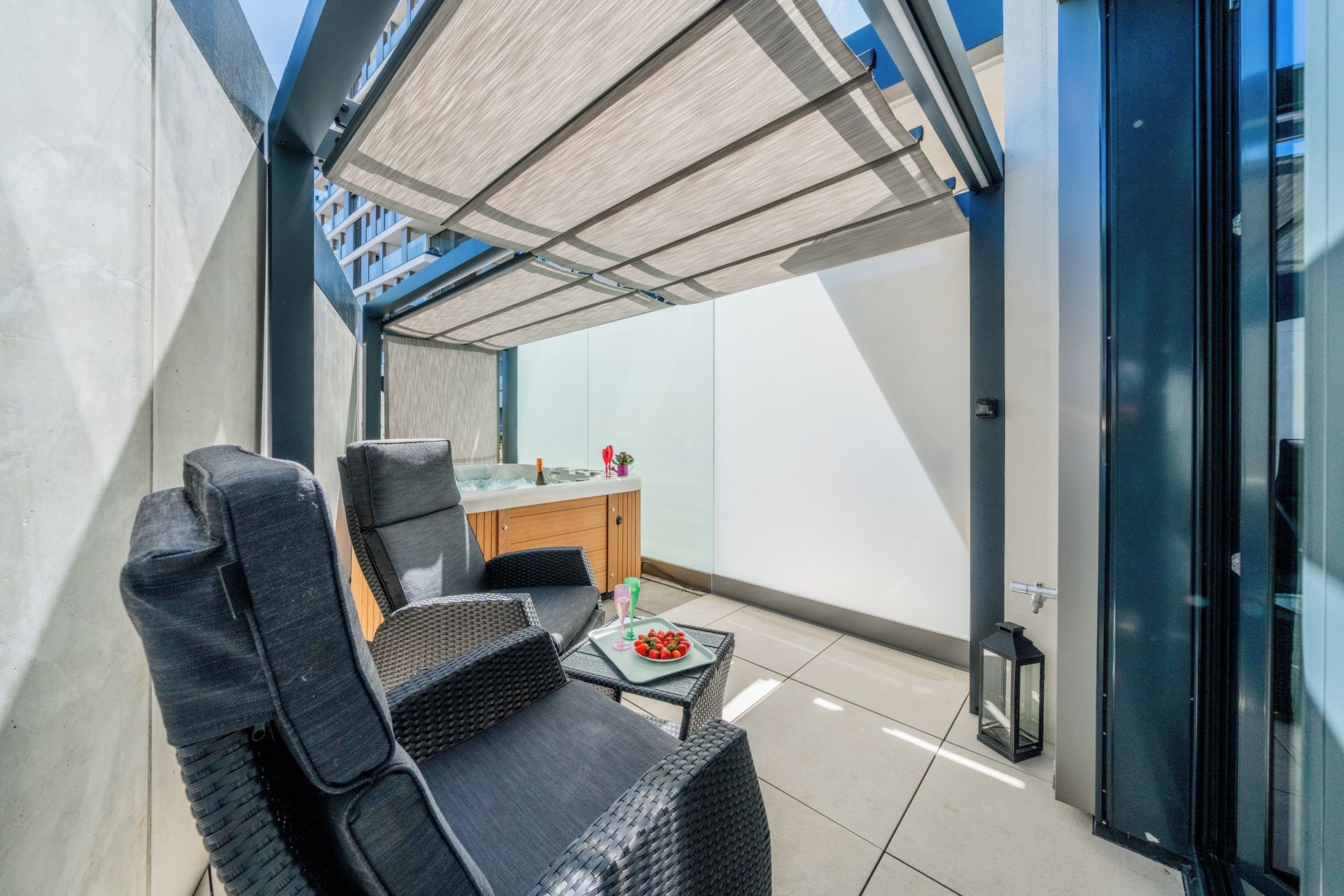 A modern outdoor seating area with a table and chairs, a hot tub, and a view of a building.