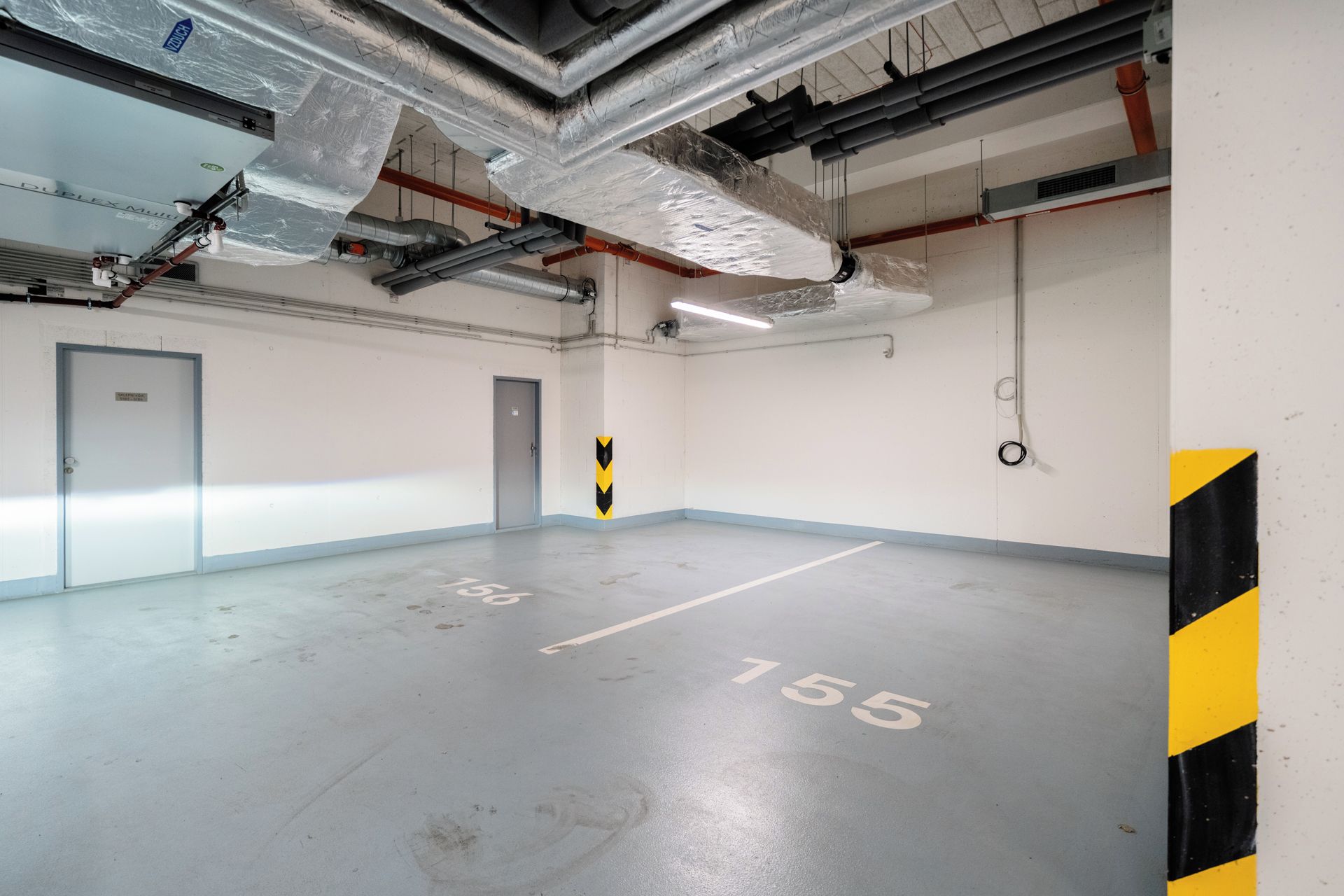 A parking garage with concrete floors, marked parking spaces, and visible ductwork on the ceiling.